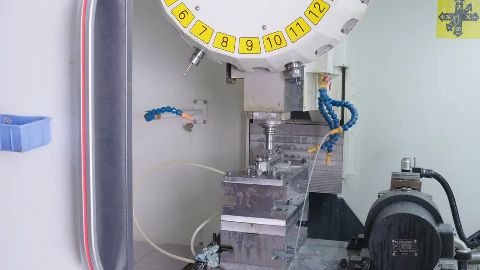 Interior of a CNC machining center with tool carousel, coolant lines, and fixtured parts
